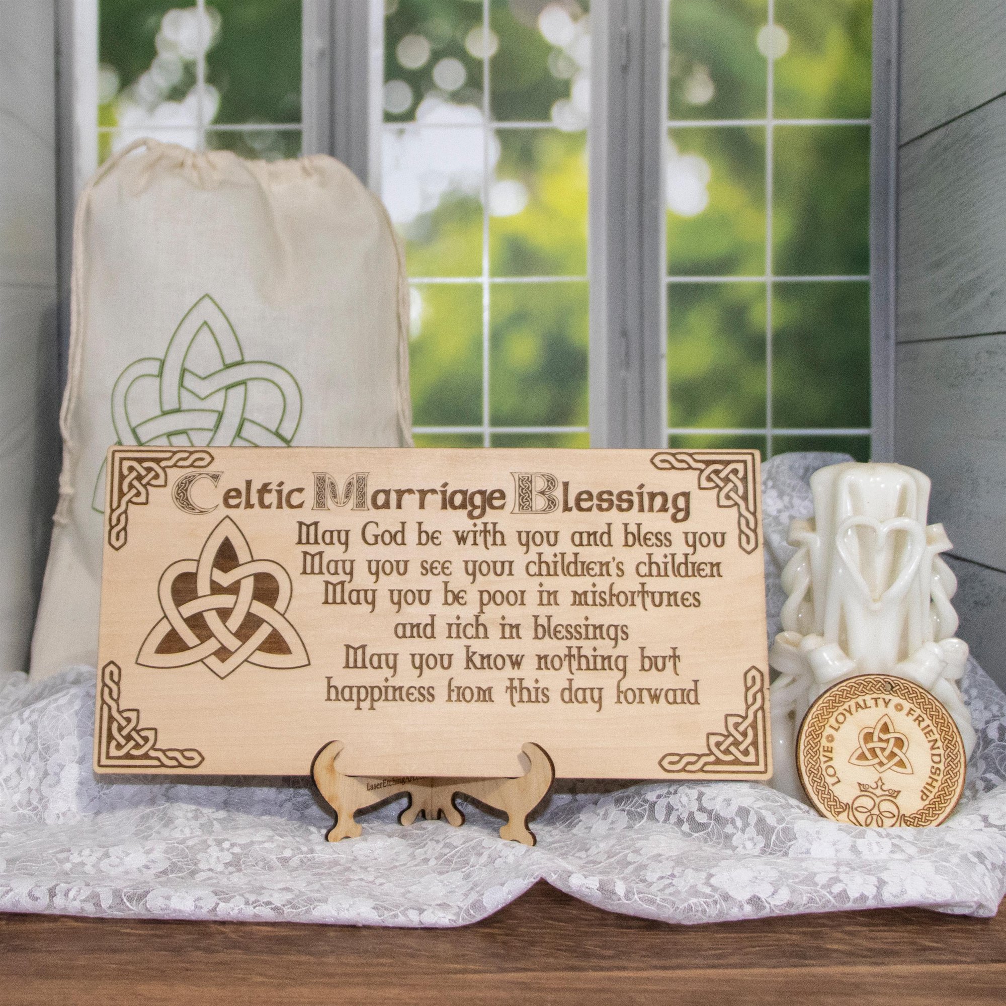 A wooden plaque engraved with a Celtic marriage blessing inside a knotwork border, on a table with candles